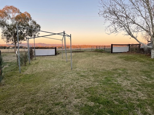 A mown paddock-side yard at sunset with hills on the horizon