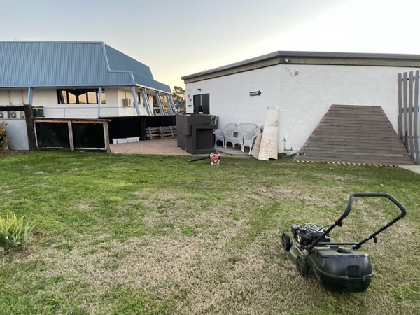 A mown back lawn at dusk with a mower parked at the edge and a house behind