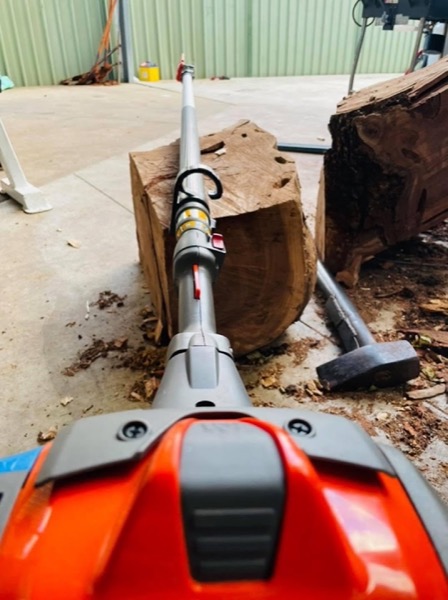 A pole saw and hand tools laid beside cut logs on a concrete slab