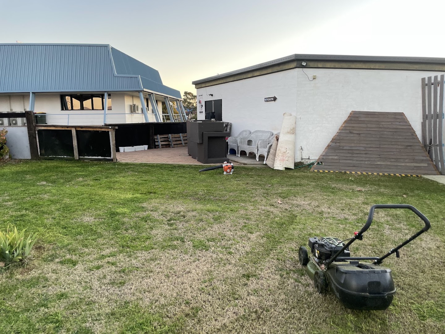A mown back lawn at dusk with a mower parked at the edge and a house behind