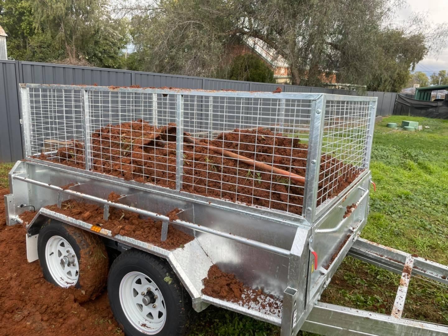 A caged trailer parked on a lawn holding a load of red mulch