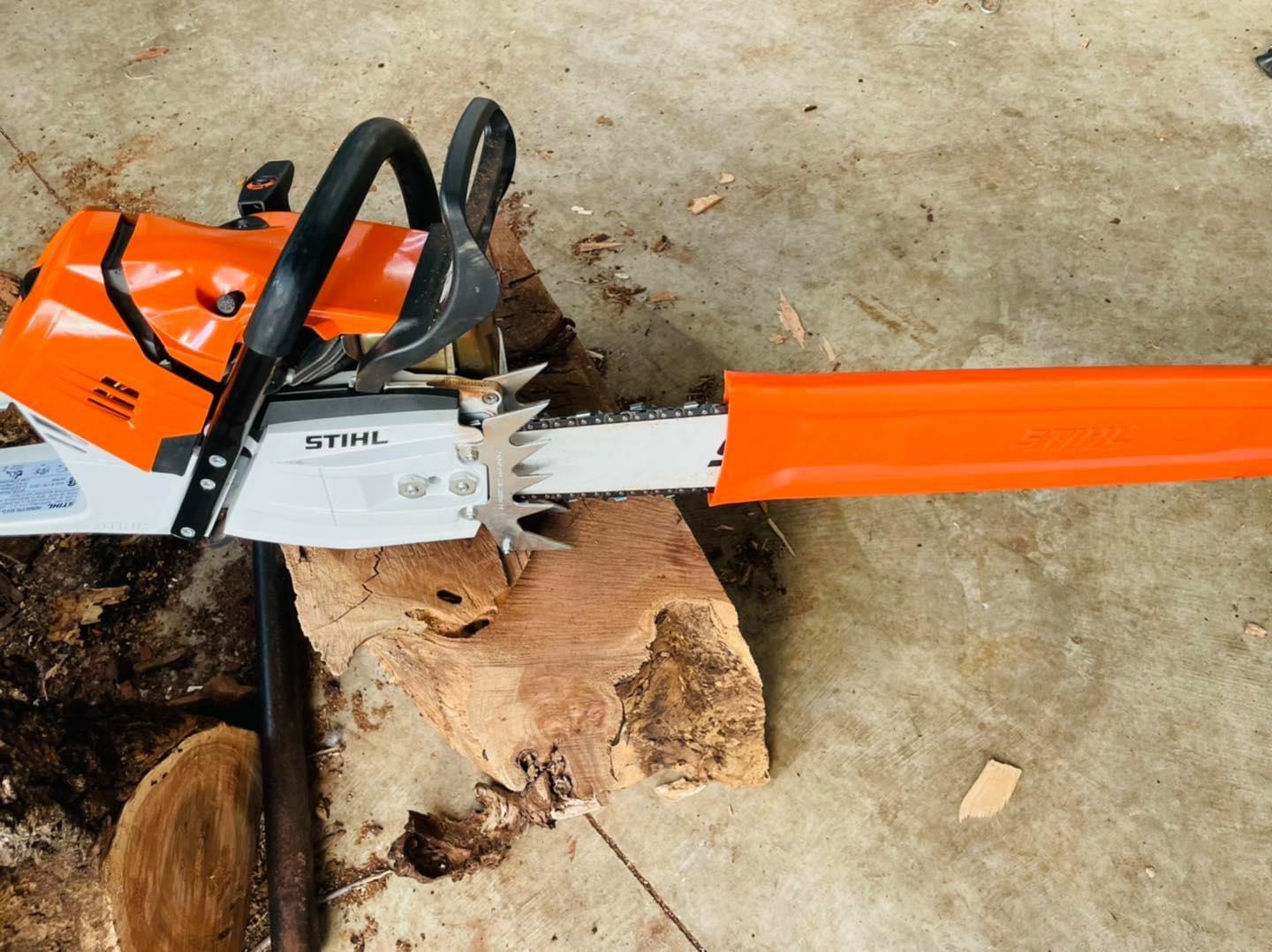 A chainsaw resting on a freshly cut timber slab beside a stump