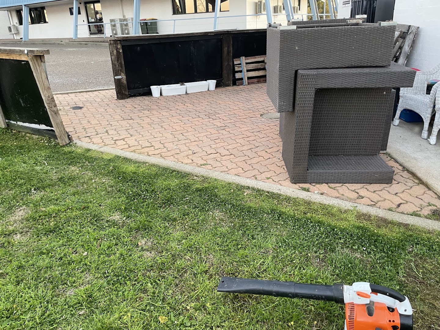 A blower resting on a swept paved courtyard beside outdoor furniture